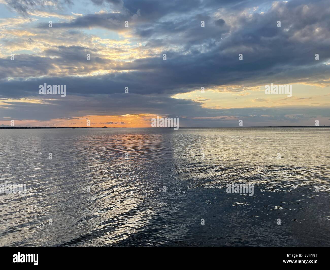 Farbenfrohe, wolkige Sonnenuntergänge spiegeln sich auf dem Wasser der Bucht - Smartphone-aufgenommenes Stockfoto