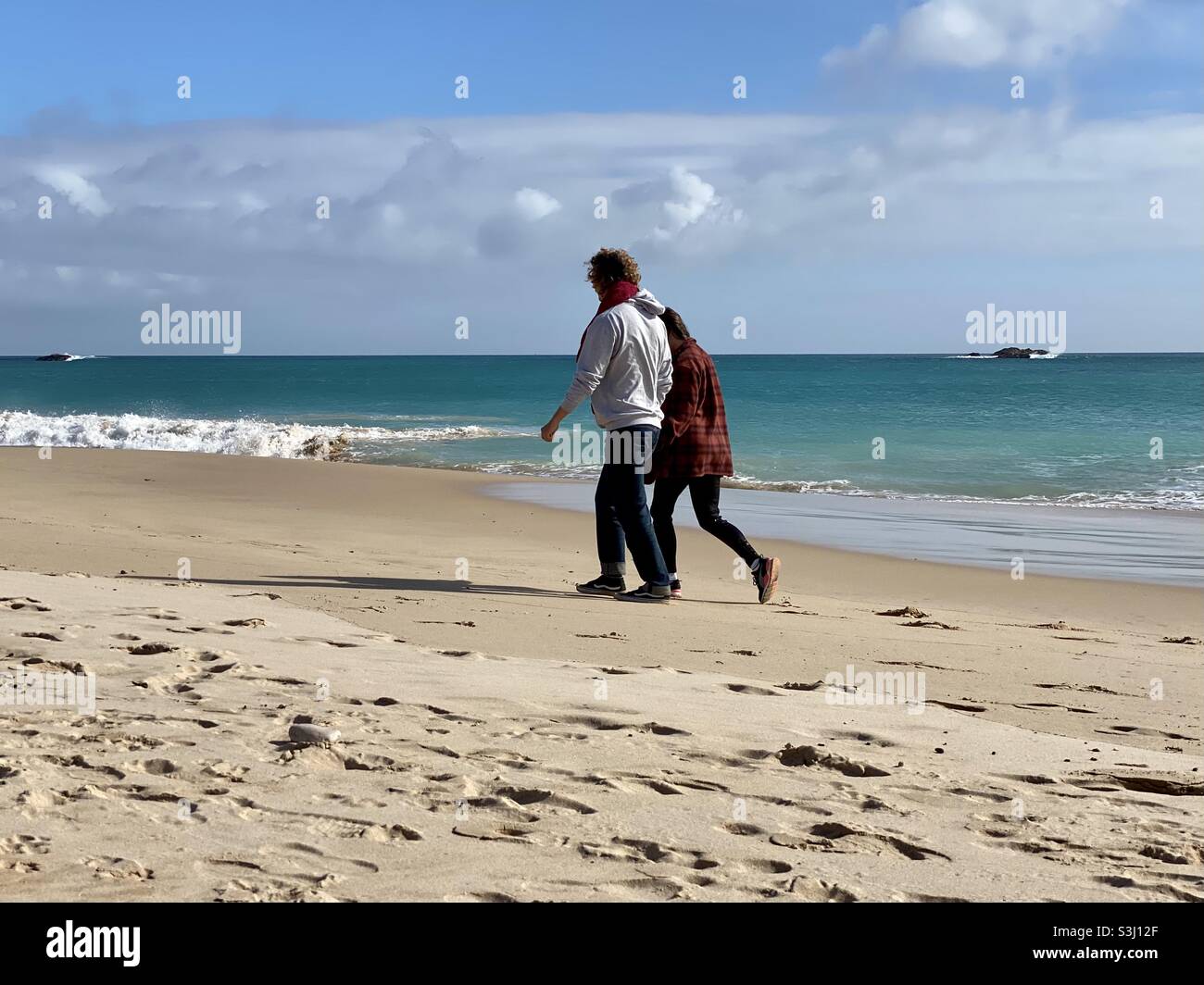Ein Paar mittleren Alters, das an einem Sandstrand entlang läuft - Smartphone-aufgenommenes Stockfoto