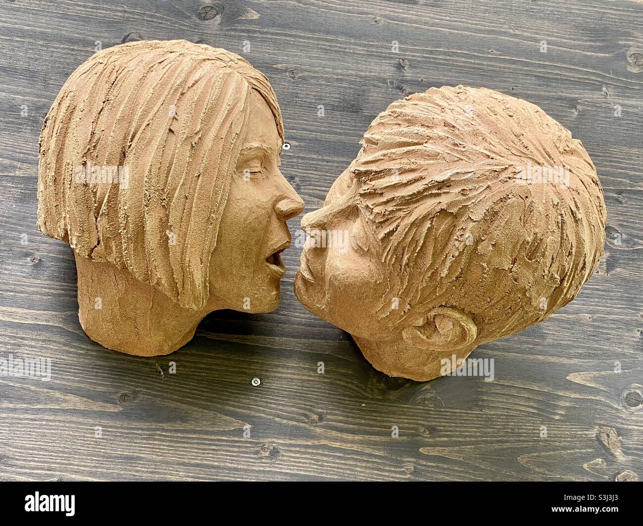 Tonskulptur zweier Gesichter, die mit hölzernem Hintergrund interagieren - Smartphone-aufgenommenes Stockfoto