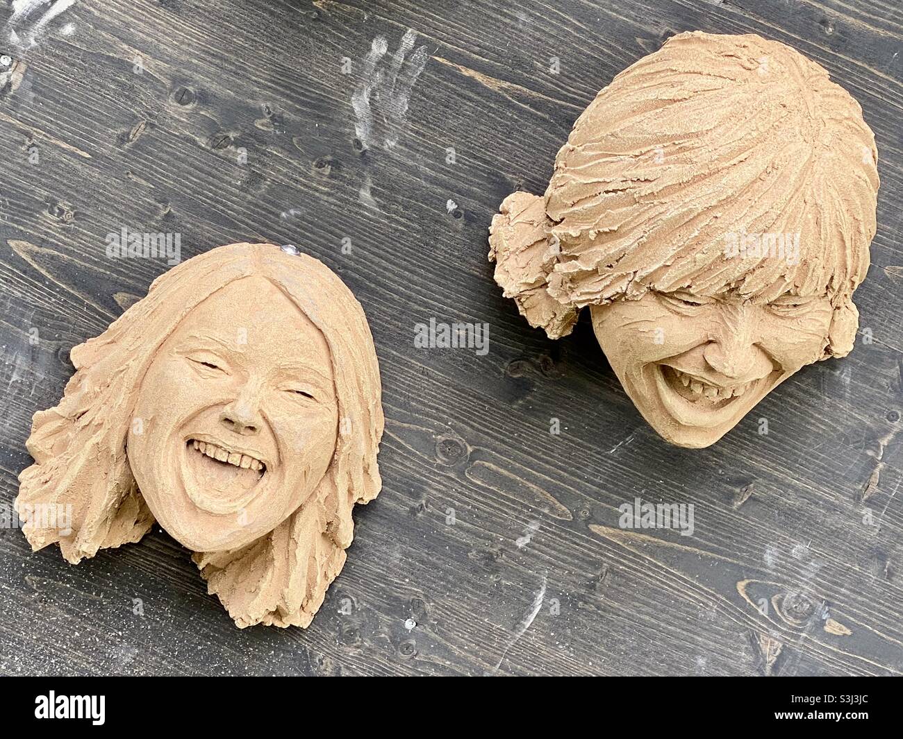 Tonskulptur zweier Gesichter, die mit hölzernem Hintergrund interagieren Stockfoto