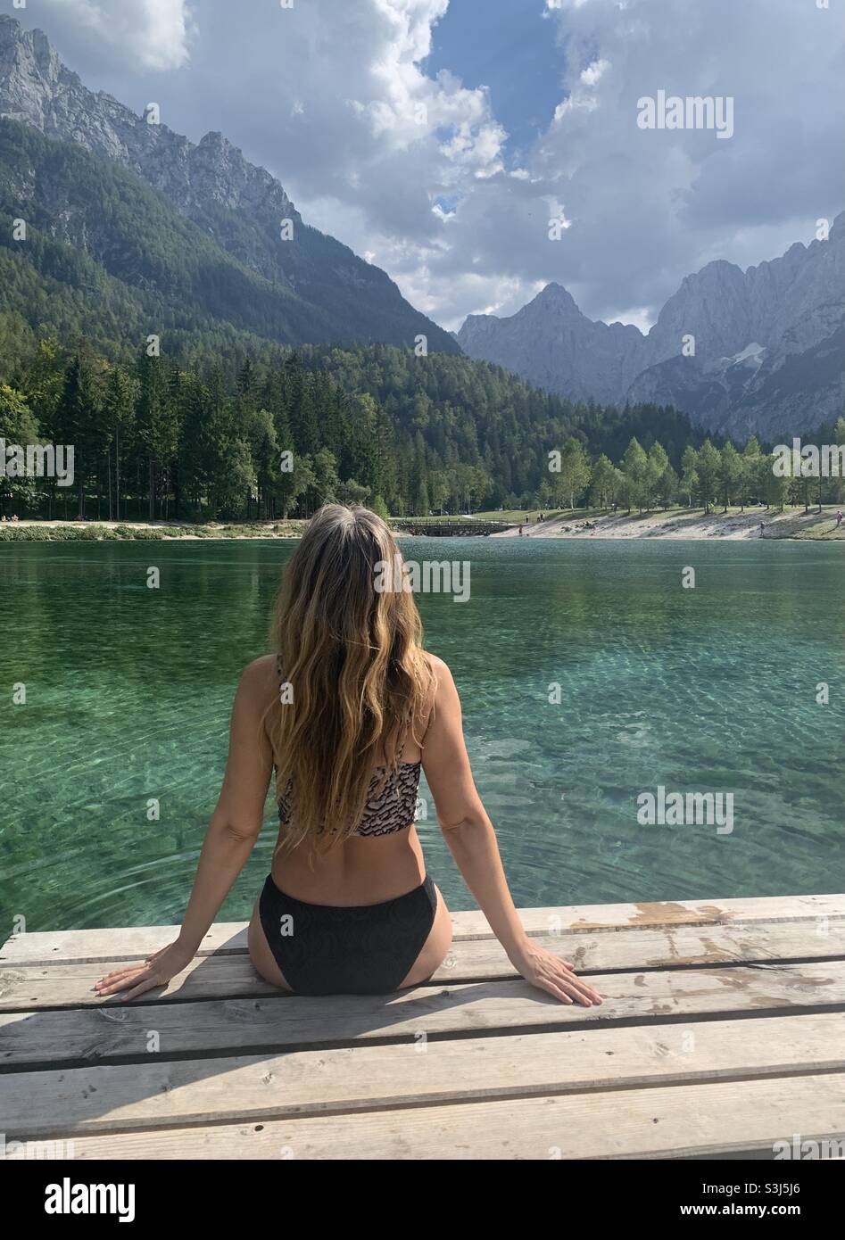 Frau, die am Ufer des Sees jasna auf einem hölzernen Pier sitzt Stockfoto