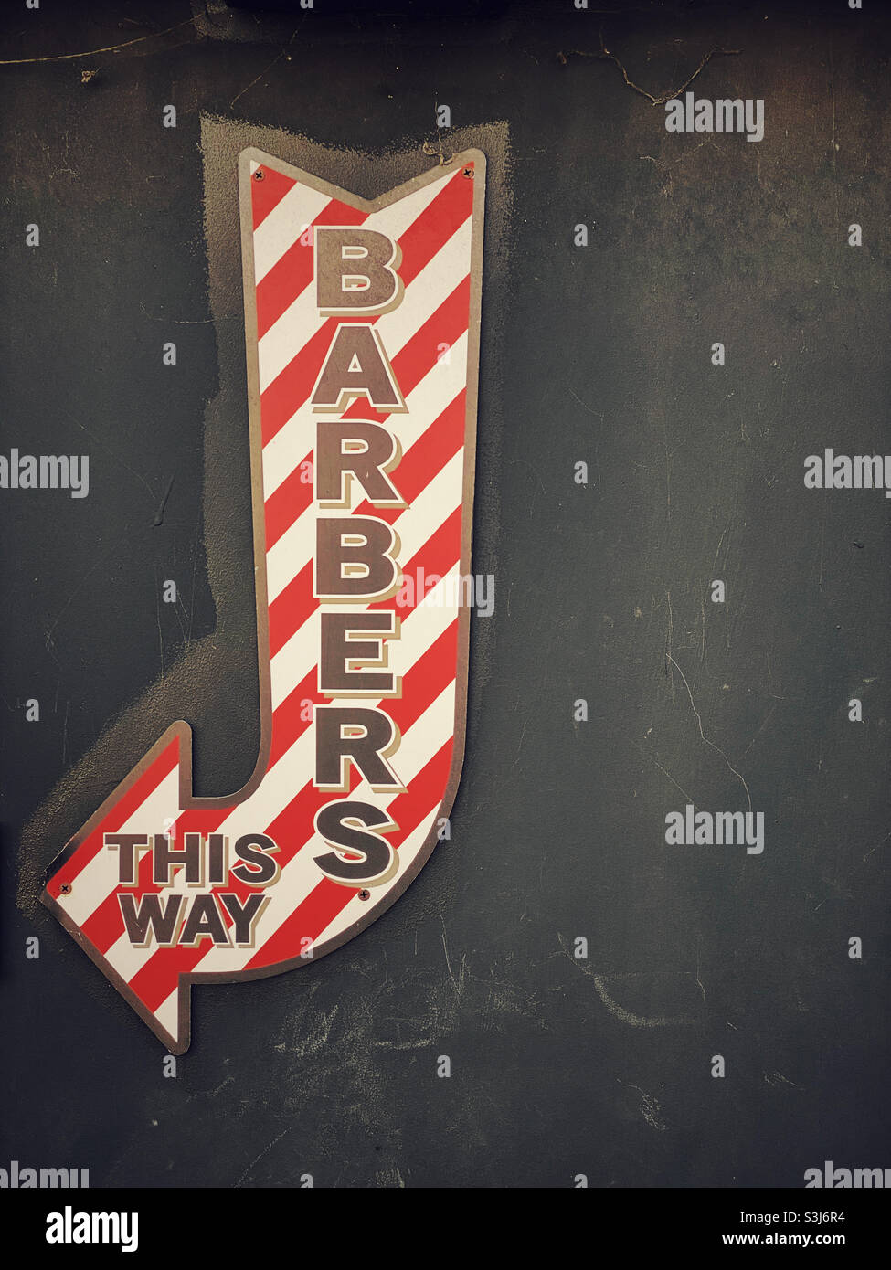 „BARBERS - THIS WAY“ das ikonische rot-weiß gestreifte Schild an einer Wand hilft, ein Unternehmen zu fördern sowie Kunden für einen Haarschnitt zu leiten. Foto ©️ COLIN HOSKINS. - Smartphone-aufgenommenes Stockfoto