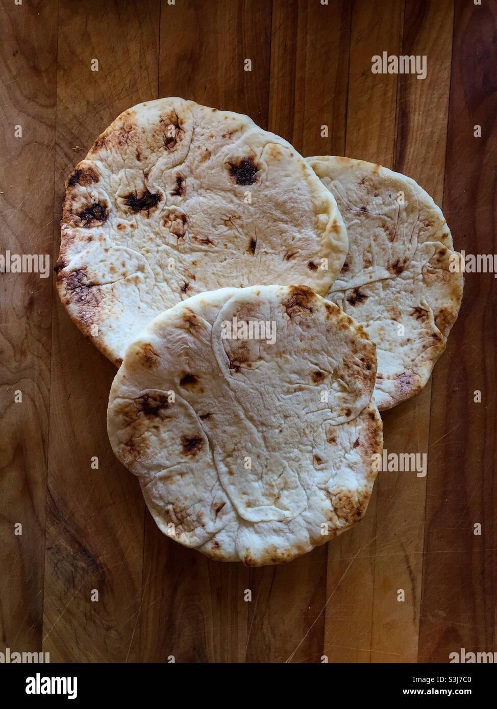 Drei leckere Naans auf einem Holzblock. Laibe aus tiefgefrorenem Flachbrot, angeordnet als ein Trio von sich kreuzenden Kreisen. Naan ist das Hauptbrot im Nahen Osten und Indien. Viele Sorten und Stile. - Smartphone-aufgenommenes Stockfoto
