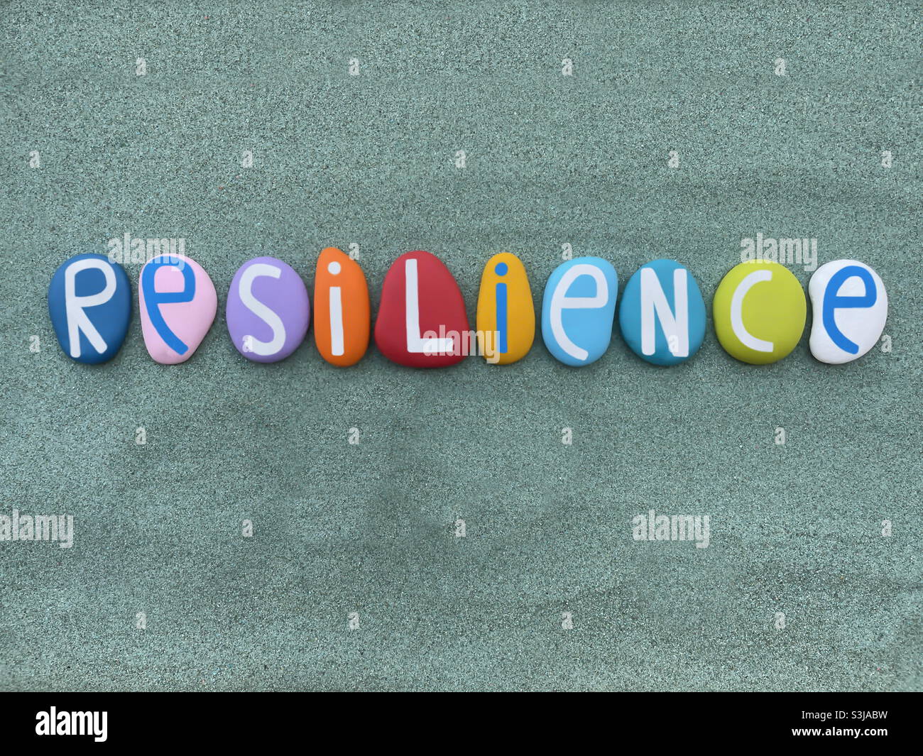 Resilienz, die Fähigkeit, wieder glücklich zu sein, nachdem etwas schwierigtes oder Schlechtes passiert ist, Kreative Textkomposition mit mehrfarbigen Steinbuchstaben über grünem Sand Stockfoto