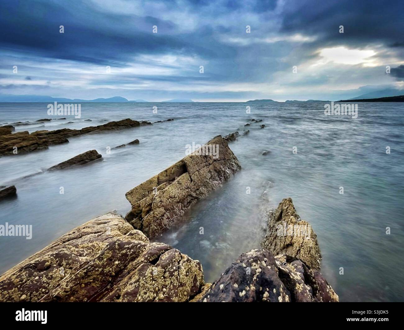 Felsen, die an der Südwestküste Irlands in Ballinskelligs Bay, Grafschaft Kerry, im August ins Meer gelangen. Stockfoto