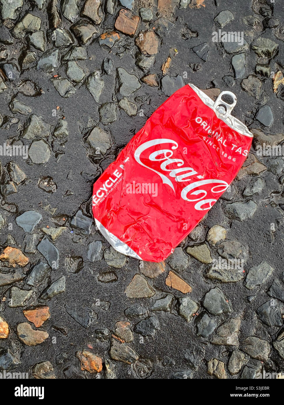 Eine zerquetschte Dose von Original Taste Coca-Cola wurde auf eine Straße geworfen. Dieses Getränk ist sehr hoch in Zucker und Kalorien. Ist es Müll?! Foto ©️ COLIN HOSKINS. - Smartphone-aufgenommenes Stockfoto
