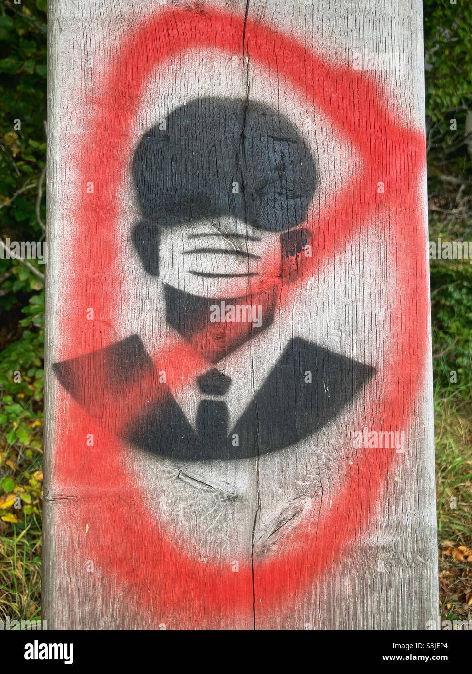 Ein Graffiti eines Mannes im Anzug, der eine Maske mit roter Linie trägt, die sie kreuzt Stockfoto