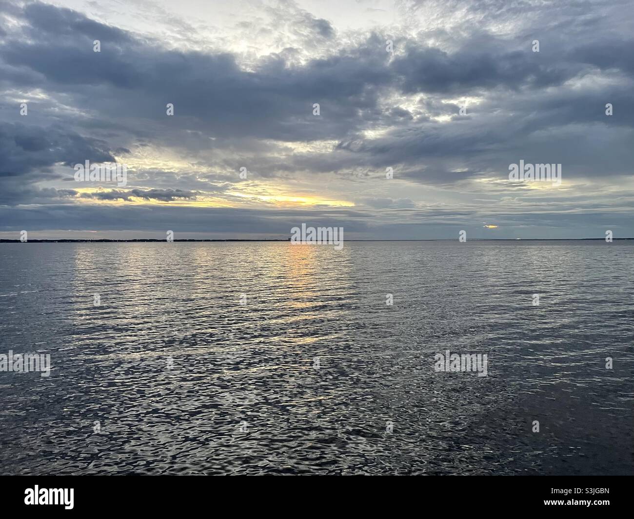 Dunkle, stürmische Sonnenuntergangswolken mit Farbreflexen auf dem Wasser Stockfoto