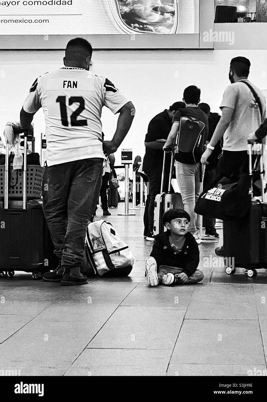 Junge, der auf dem Boden im Flughafen sitzt Stockfoto