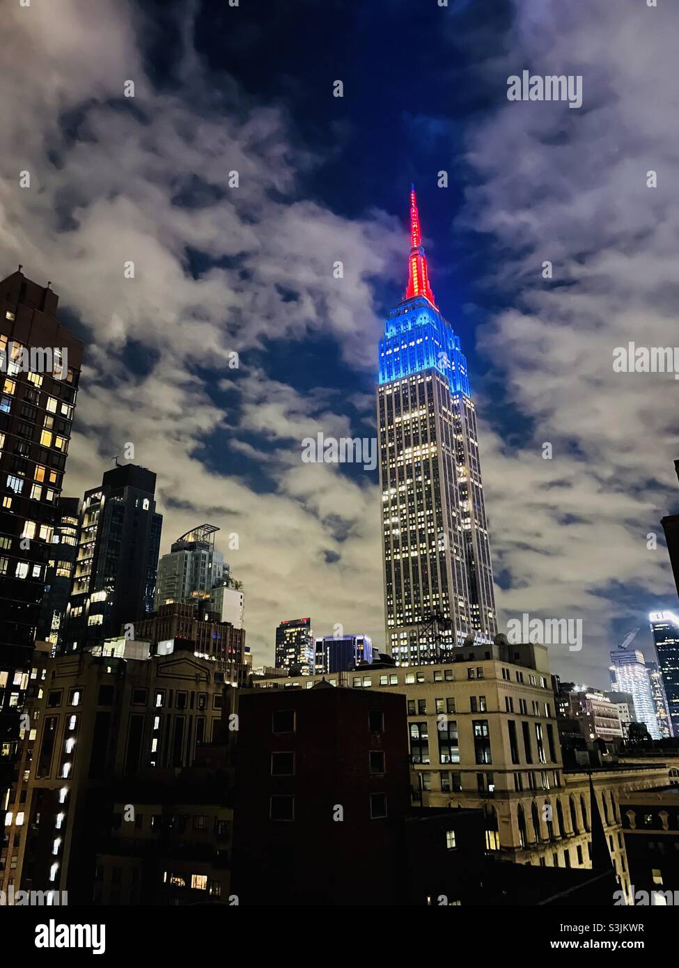 Das Empire State Building mit rot-weißen und blauen Lichtern vor einem bewölkten Nachthimmel - Smartphone-aufgenommenes Stockfoto