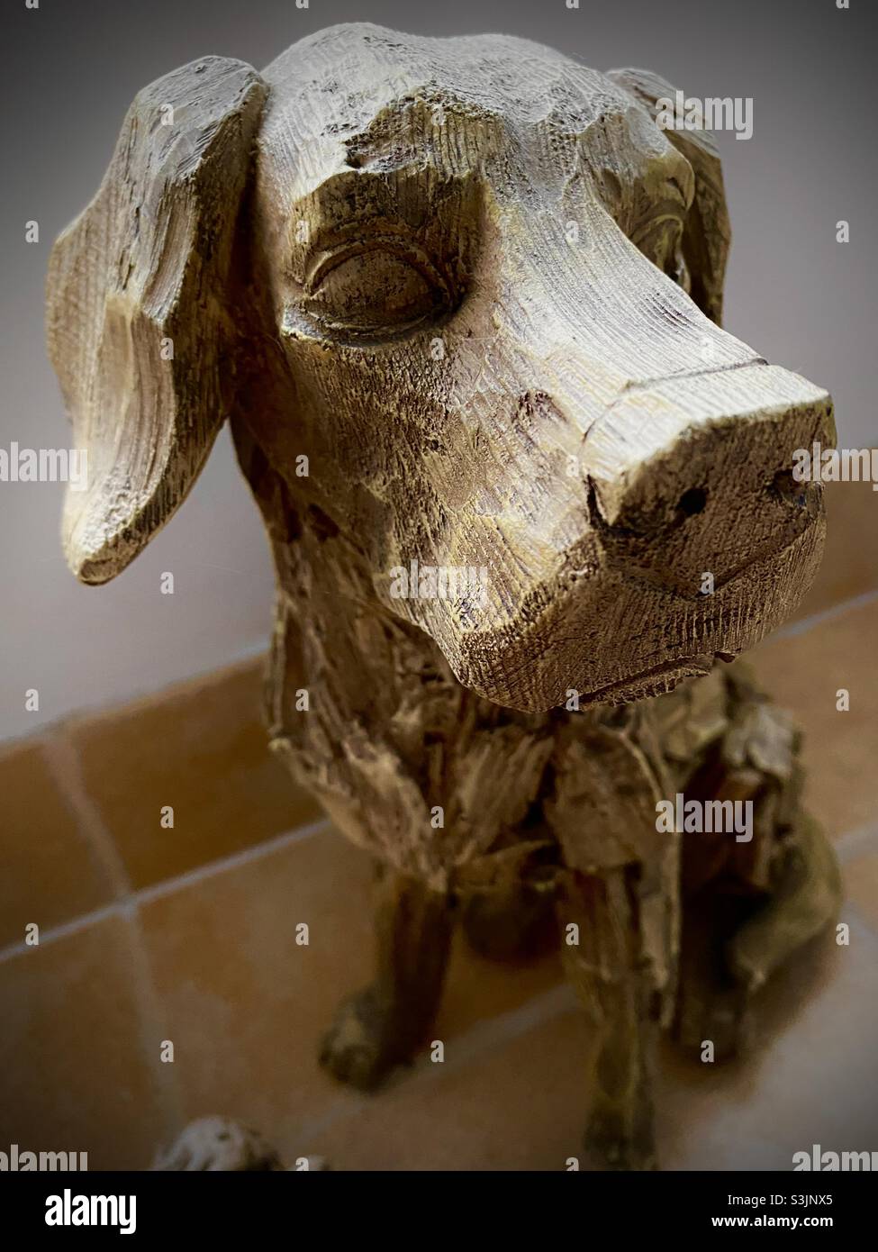 Handgeschnitzte Holzstatue eines labrador-Welpen, der auf einem gefliesten Innenboden sitzt - Smartphone-aufgenommenes Stockfoto