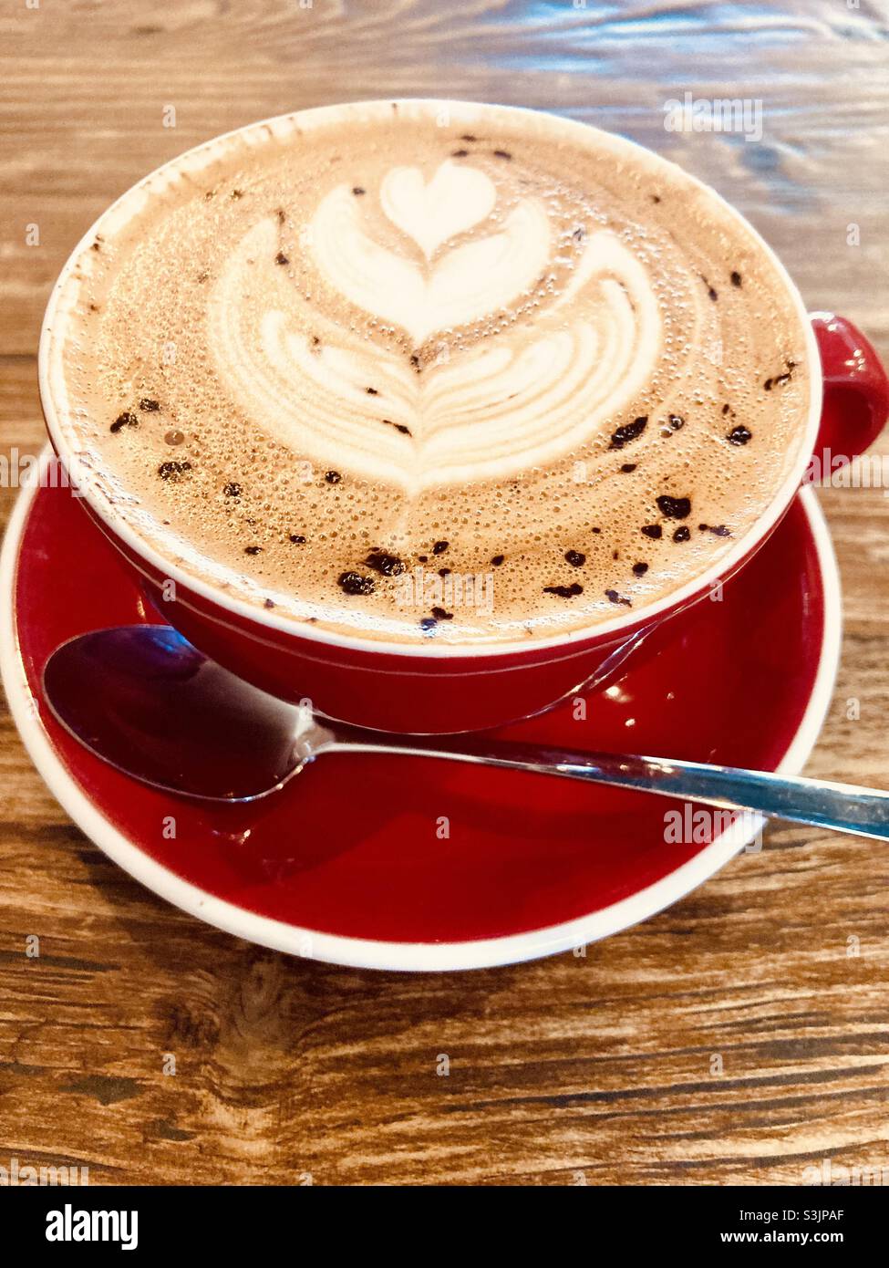 Kaffeekunst, handwerklicher Cappuccino-Kaffee in einer roten Tasse mit Untertasse Stockfoto