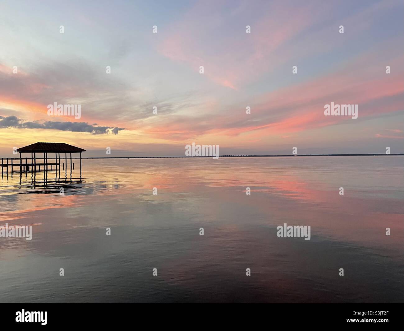 Farbenfrohe, pastellfarbene Sonnenuntergänge über dem ruhigen Wasser der Bucht mit Bootsanlegestelle und Reflexionen Stockfoto