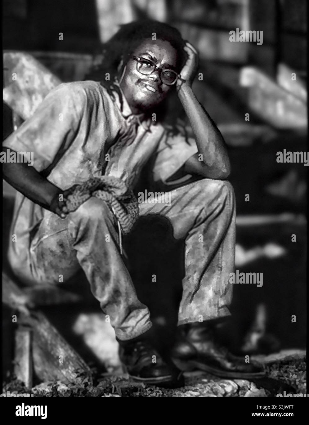 Ein junger jamaikanischer Mann, der auf einer Stufe im ländlichen Jamaika sitzt. - Smartphone-aufgenommenes Stockfoto