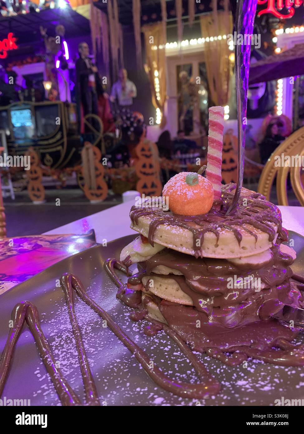 Stapel von Pfannkuchen mit Schokoladensauce bedeckt mit Halloween-Figuren im Hintergrund Stockfoto