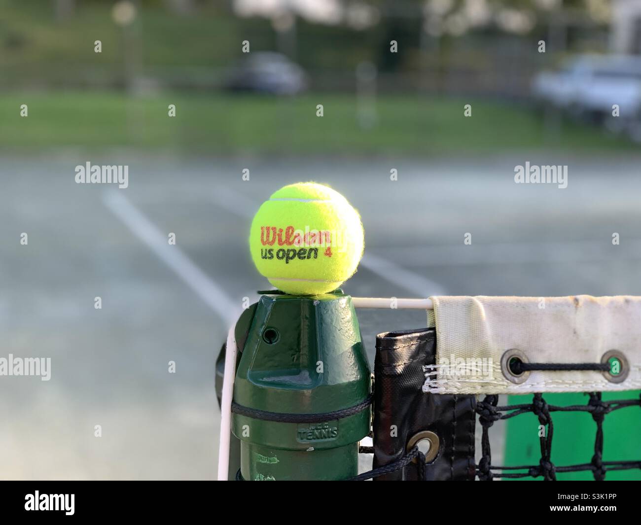 Einzeltennisball Wilson US öffnen 4 am Rand des Netzes, gelb, mit Tennisplatz Hintergrund. Stockfoto