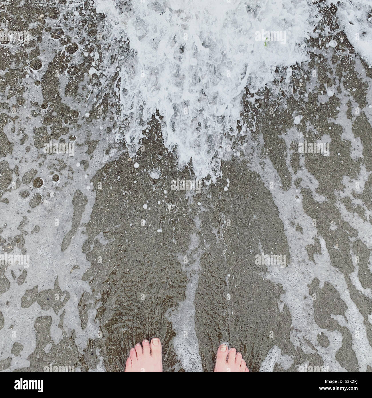 Stehen am Rande des Wassers an einem Strand - Smartphone-aufgenommenes Stockfoto