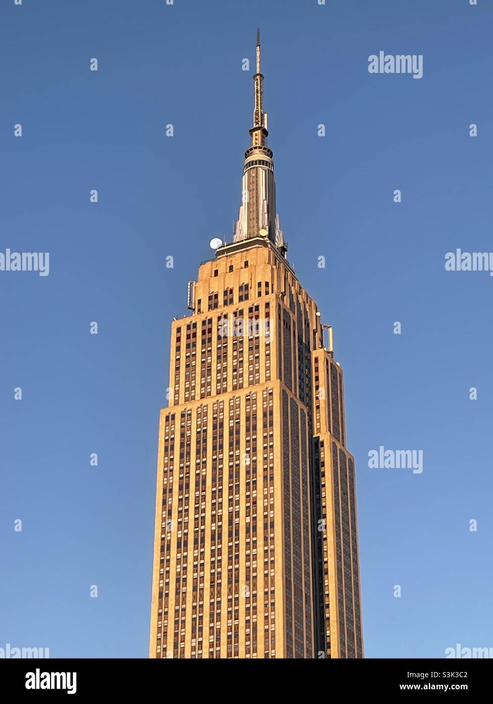 Im frühen Morgenlicht nähert sich der Mond der Spitze des Empire State Building in New York City Stockfoto