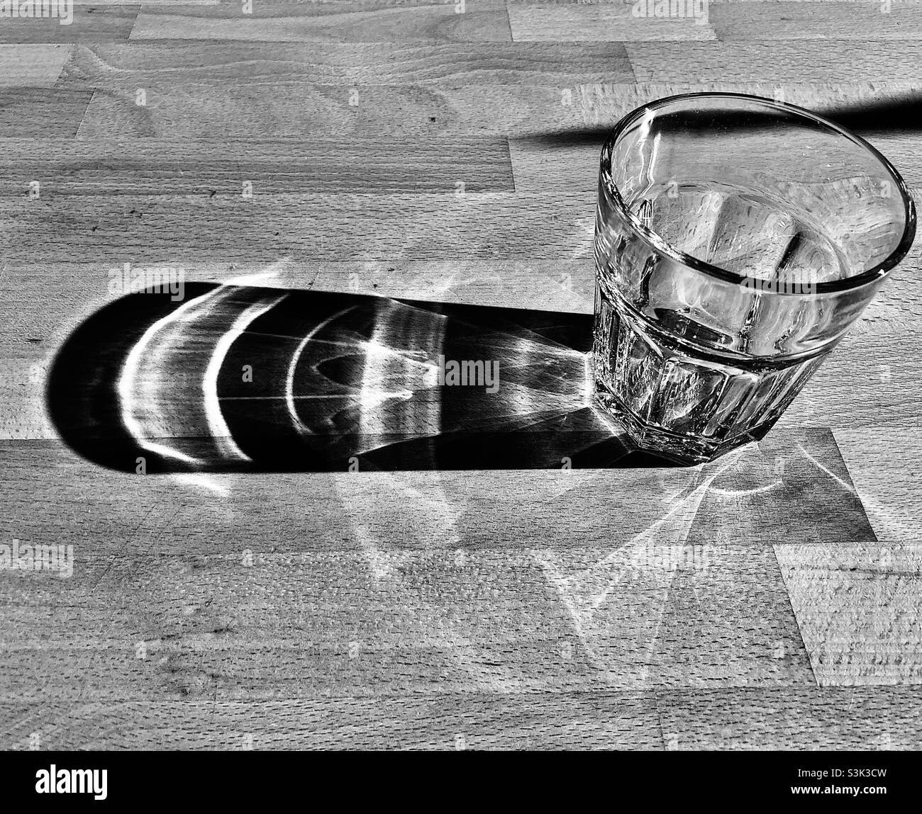 Ein Glas steht auf dem Holztisch und wirft einen langen Schatten - Smartphone-aufgenommenes Stockfoto