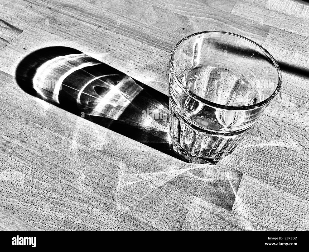 Ein Glas steht auf dem Holztisch und wirft einen langen Schatten Stockfoto