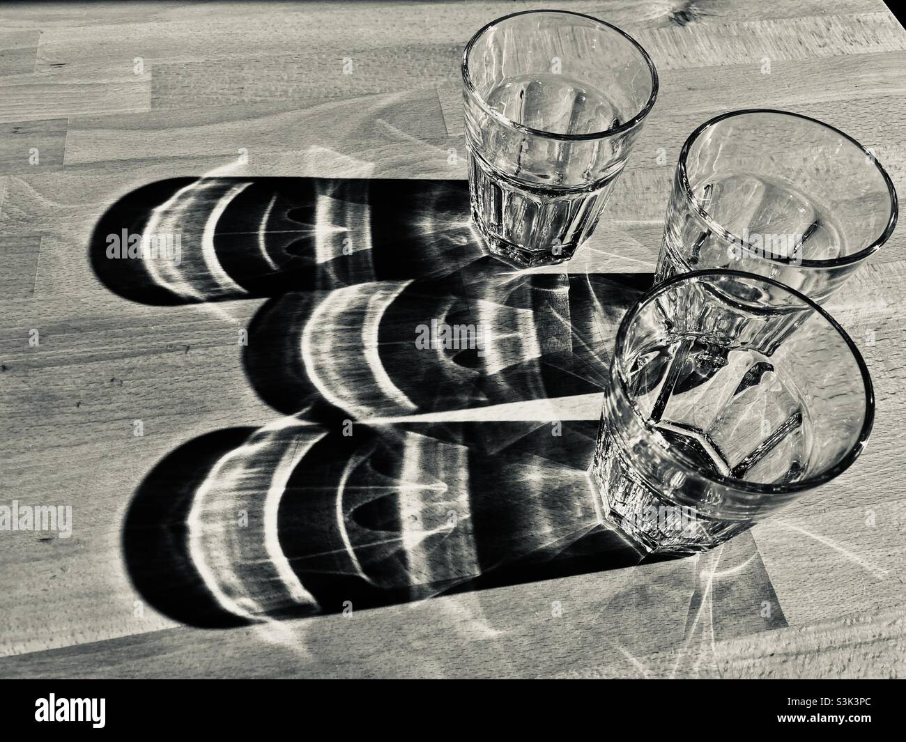 Drei Glas Wasser stehen auf einem Holztisch und werfen lange Schatten Stockfoto