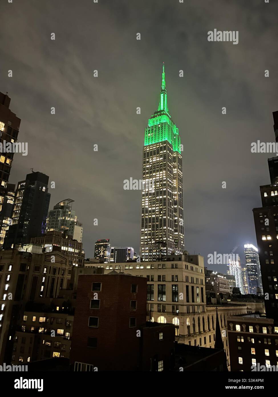 Der Turm leuchtet auf dem Empire State Building dicht grün vor einem regnerischen Nachthimmel Stockfoto