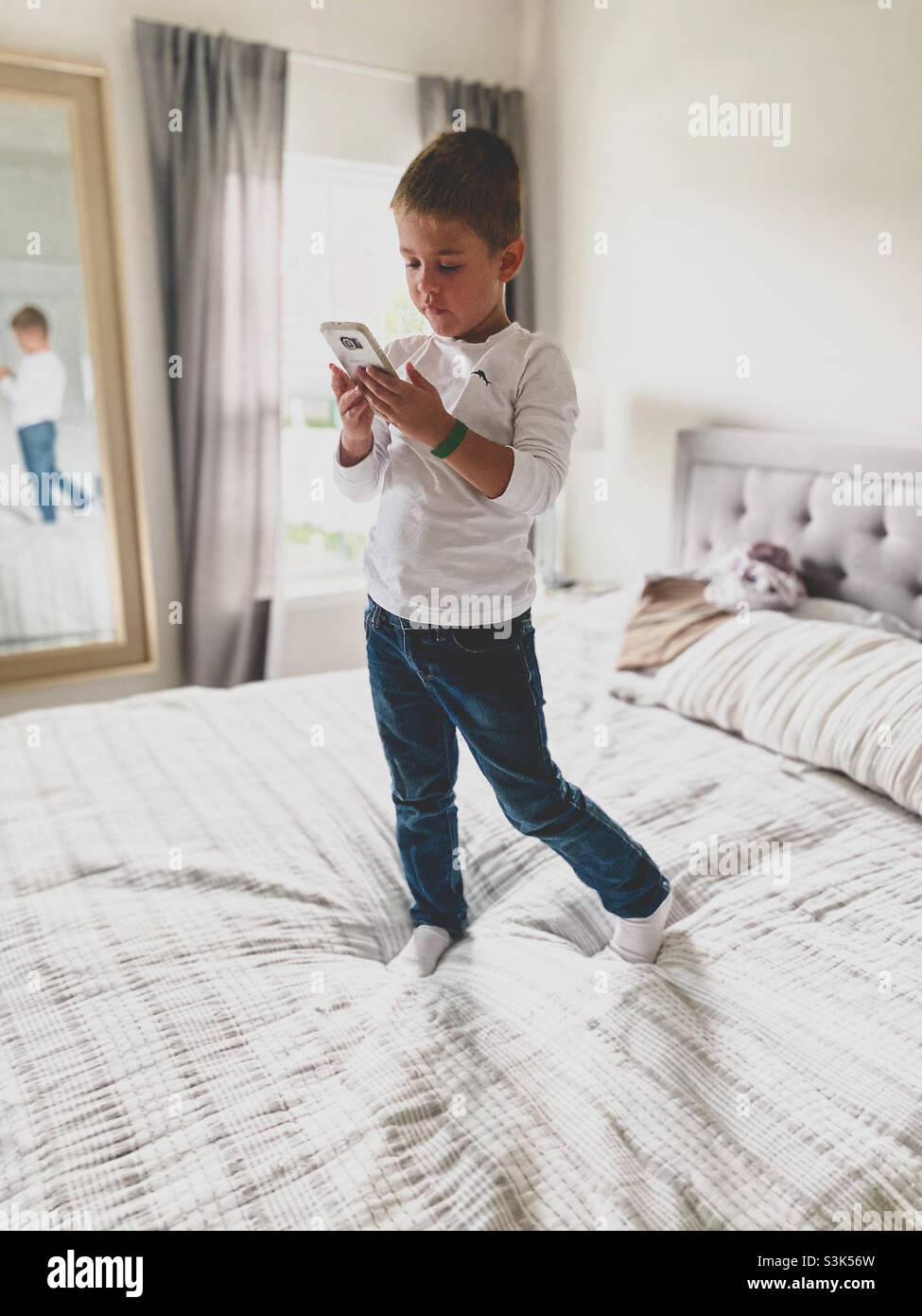 Kleiner Junge, der auf einem großen Doppelbett am Telefon spielt Stockfoto