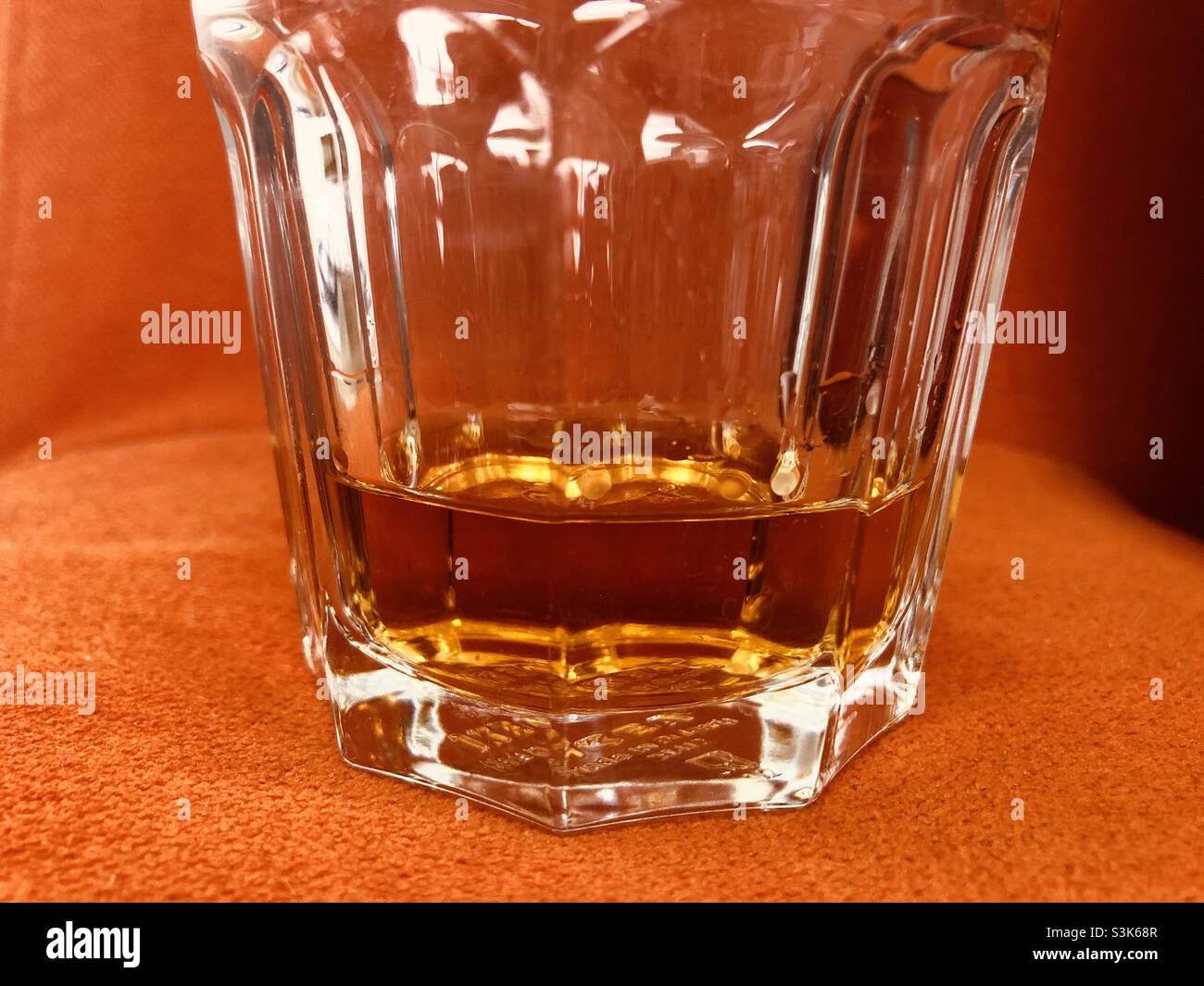 Nahaufnahme eines Glases Whisky auf einer leuchtend orangefarbenen Oberfläche Stockfoto