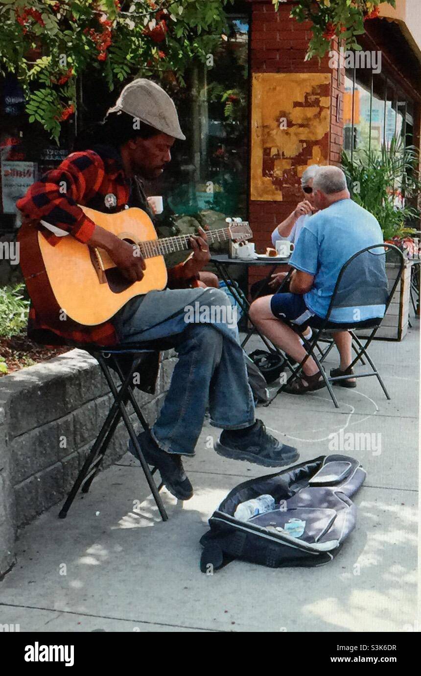 Street Photography, Kensington in Calgary, Alberta , Entertainer, Busker, Musiker, Gitarrist, Sänger , Gitarrenkoffer, Bargeld, Geld - Smartphone-aufgenommenes Stockfoto