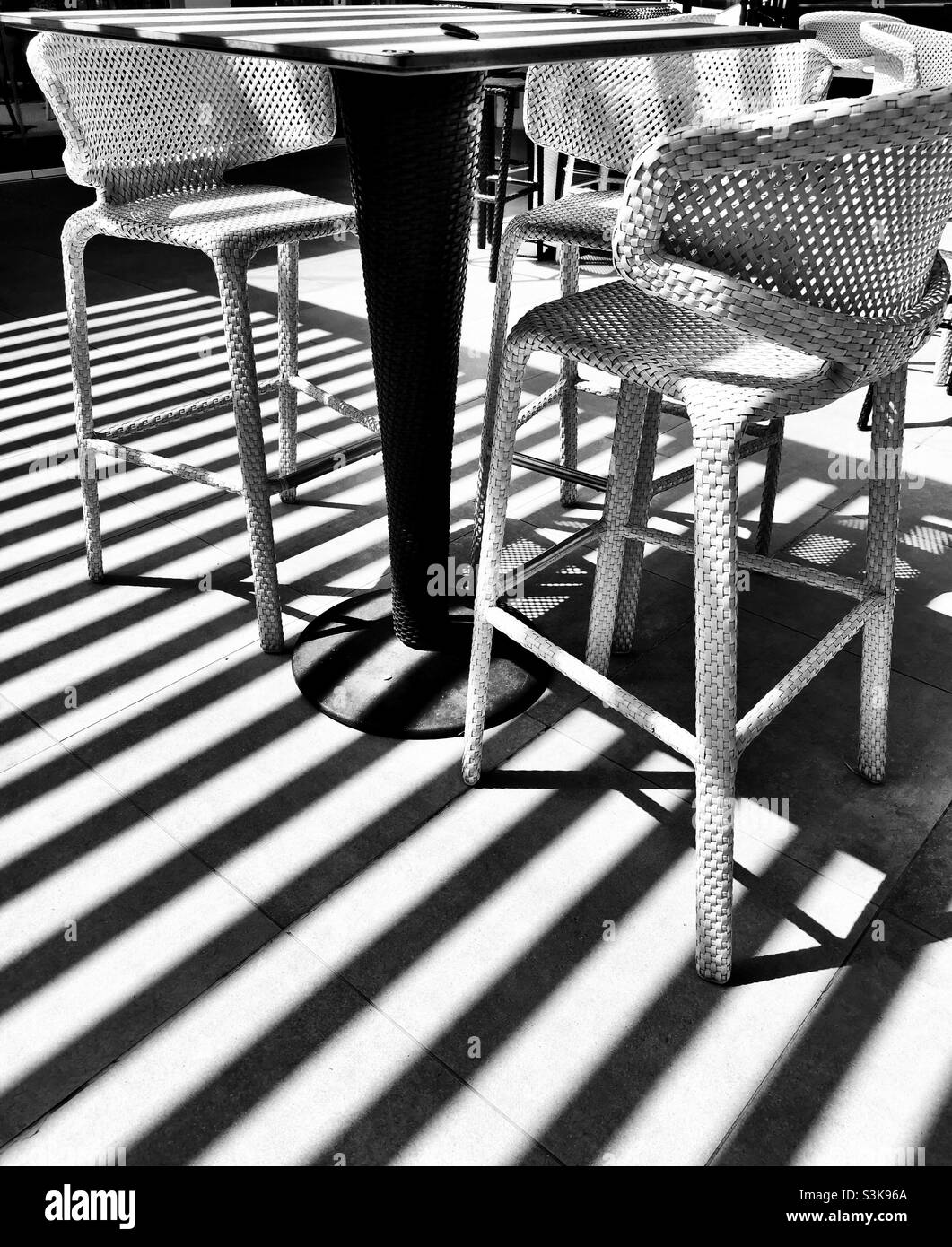 Schwarz-weiße Barhocker unter dem Schatten eines gestreiften Pergola-Dachs Stockfoto