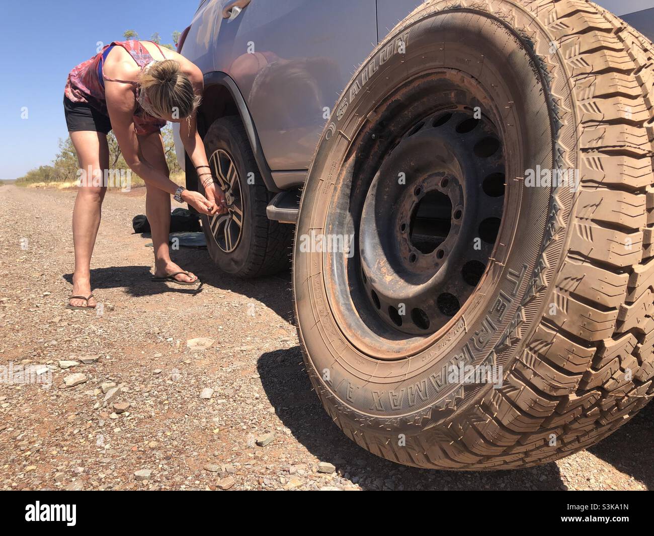 Eine Frau wechselt auf einer staubigen Outback-Straße in Westaustralien einen Reifen - Smartphone-aufgenommenes Stockfoto