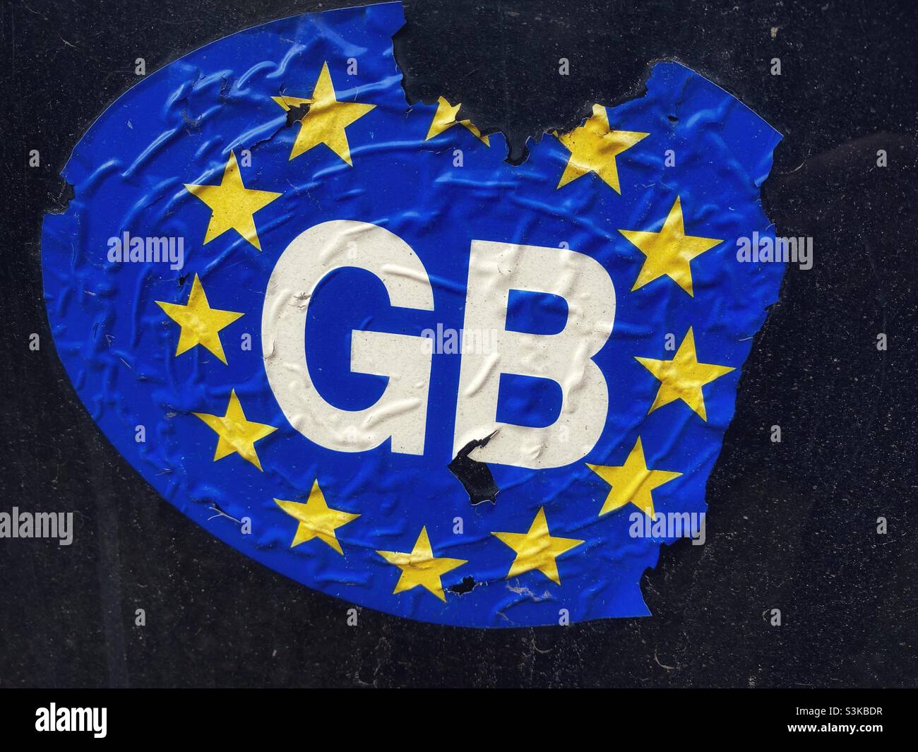 Ein zerrissener GB-Autoaufkleber auf der Rückseite eines Autos. Der Aufkleber für Großbritannien (GB) ist nicht mehr gültig und wurde durch einen Aufkleber mit der Aufschrift ‘UK’ ersetzt - Smartphone-aufgenommenes Stockfoto