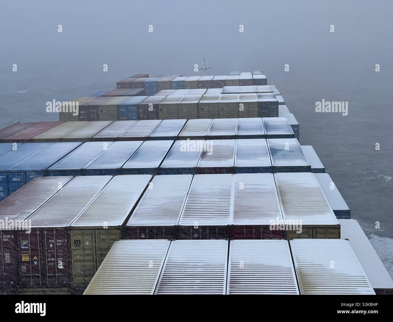 Kleine Schneeschicht auf Containern, die auf einem Handelsschiff geladen und verstaut wurden, das während des Schneefalls durch den Pazifischen Ozean über Aleutian während der Wintersaison segelt. Stockfoto