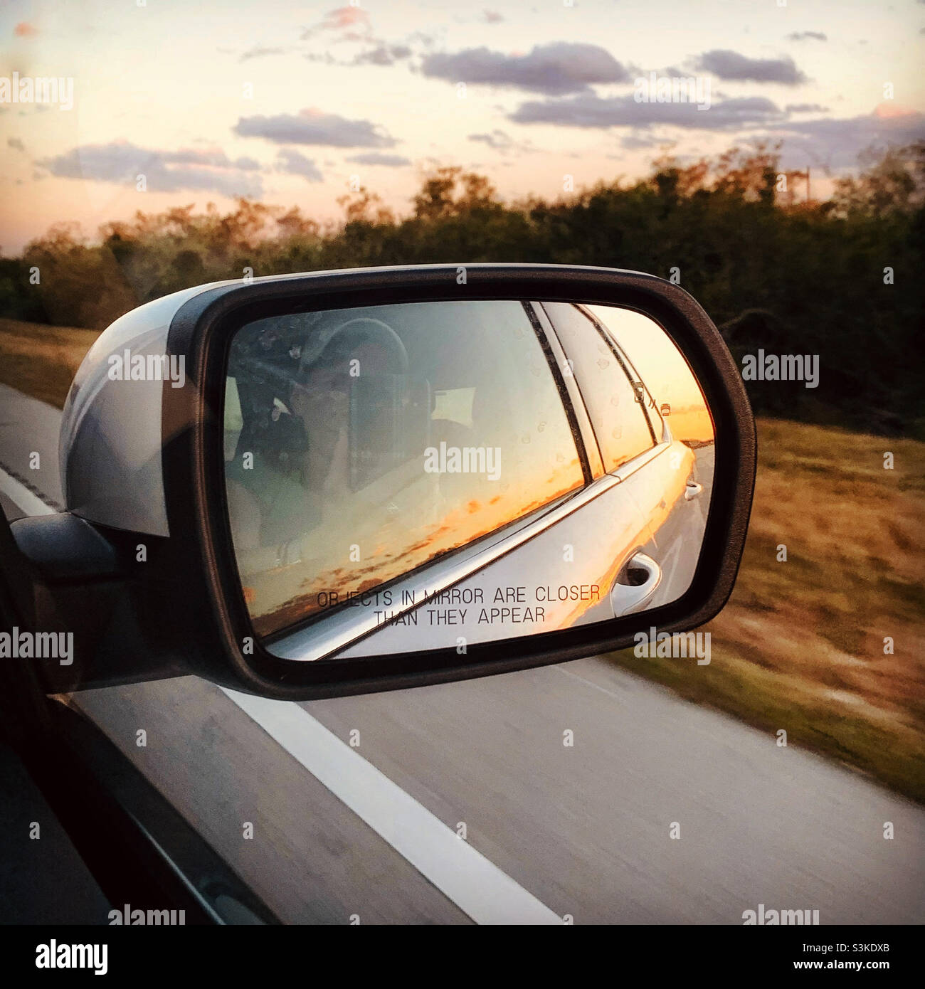 Sonnenuntergang spiegelt sich in einem Auto Rückspiegel. Roadtrip. Reisezeit. Stockfoto