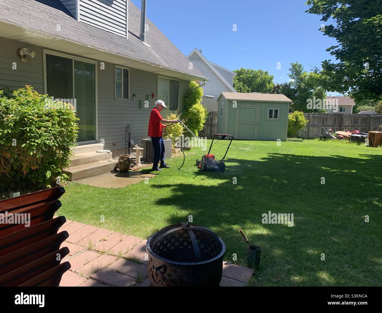 Während das Wetter in Utah, USA, aufwärmt, wird ein Mann gesehen, wie er einen Mäher in seinem Garten abspült, als Teil einer Frühjahrsreinigung. - Smartphone-aufgenommenes Stockfoto