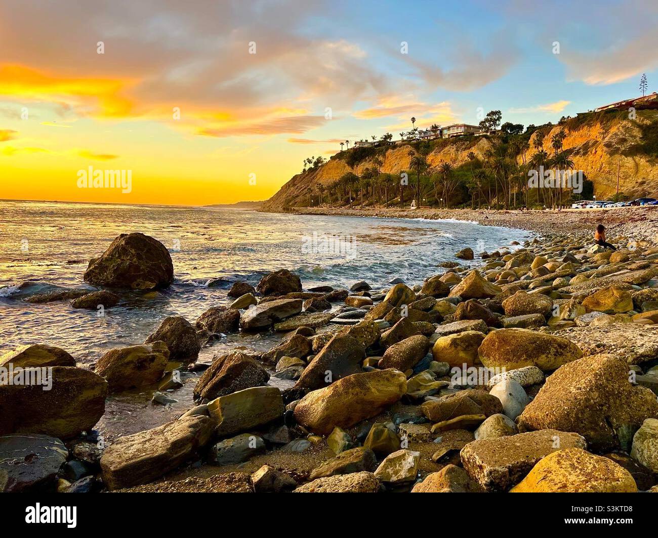 Der goldene Glanz des Sonnenuntergangs auf Strandbrocken und Klippen Stockfoto