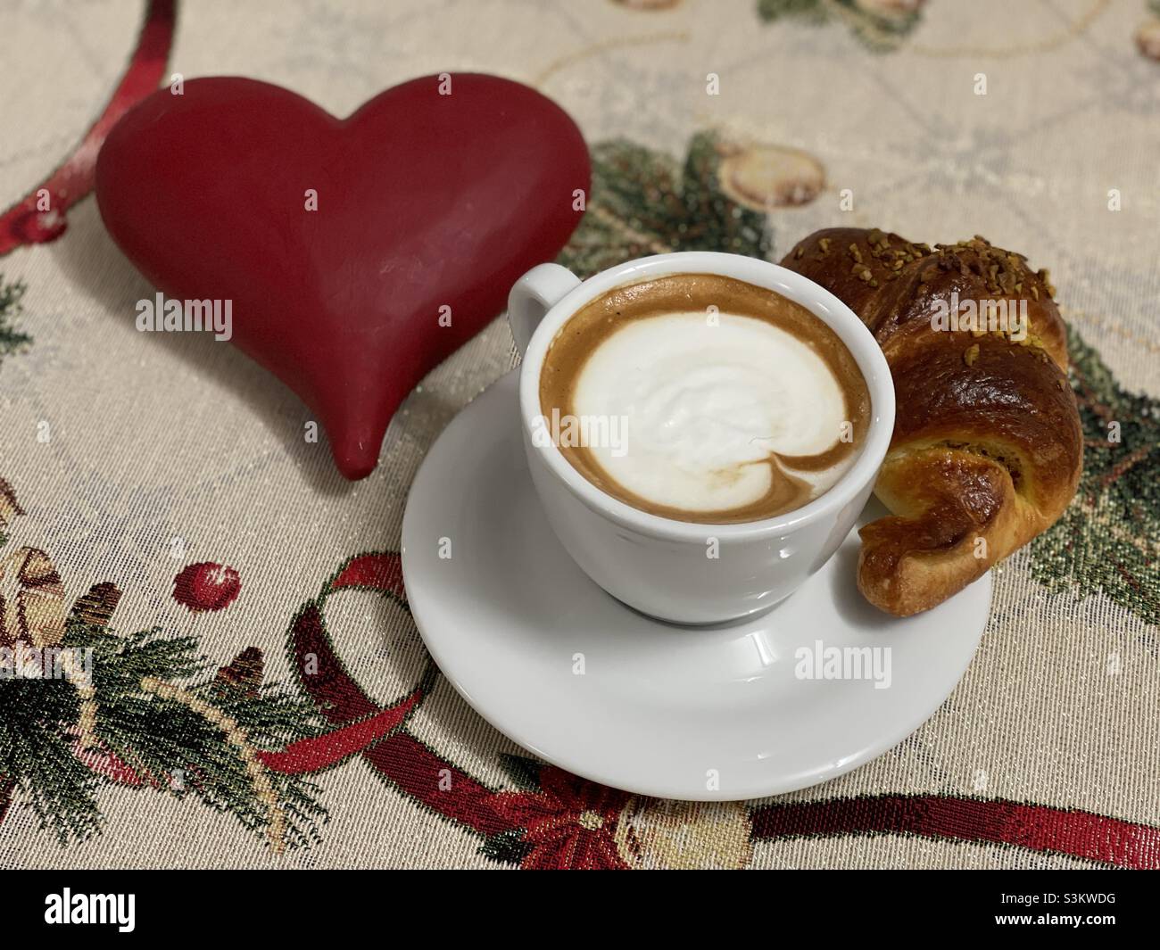 Schönes Weihnachtsfrühstück mit einem großen Steinherz, Cappuccino und Croissant an der Bar Stockfoto