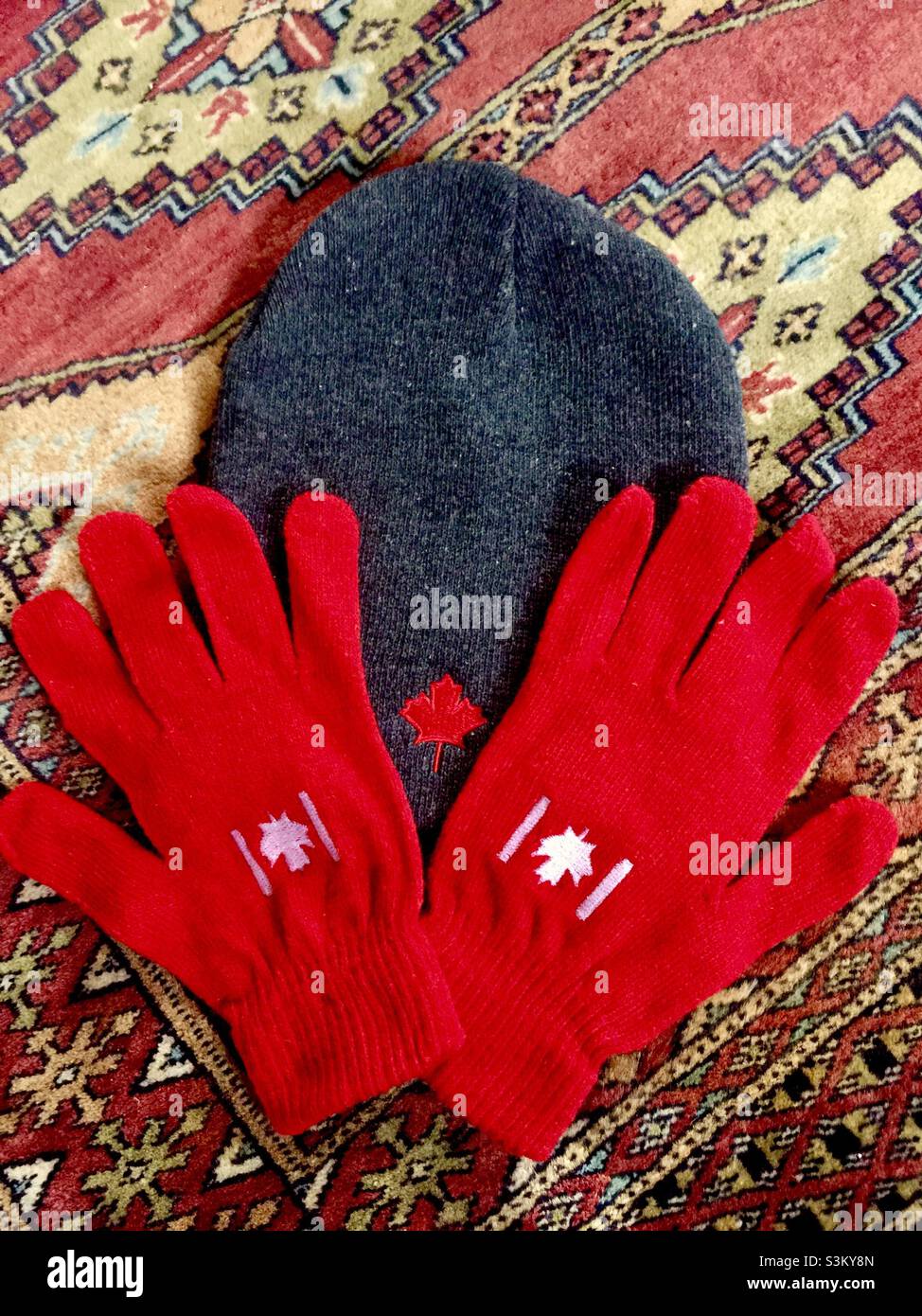 Bereit für den Winter. Kanadisches Ahornblatt-Emblem auf Handschuhen und Hut. Auf orientalischen Teppichtischdecken arrangiert. Warme Töne und Design. Stockfoto