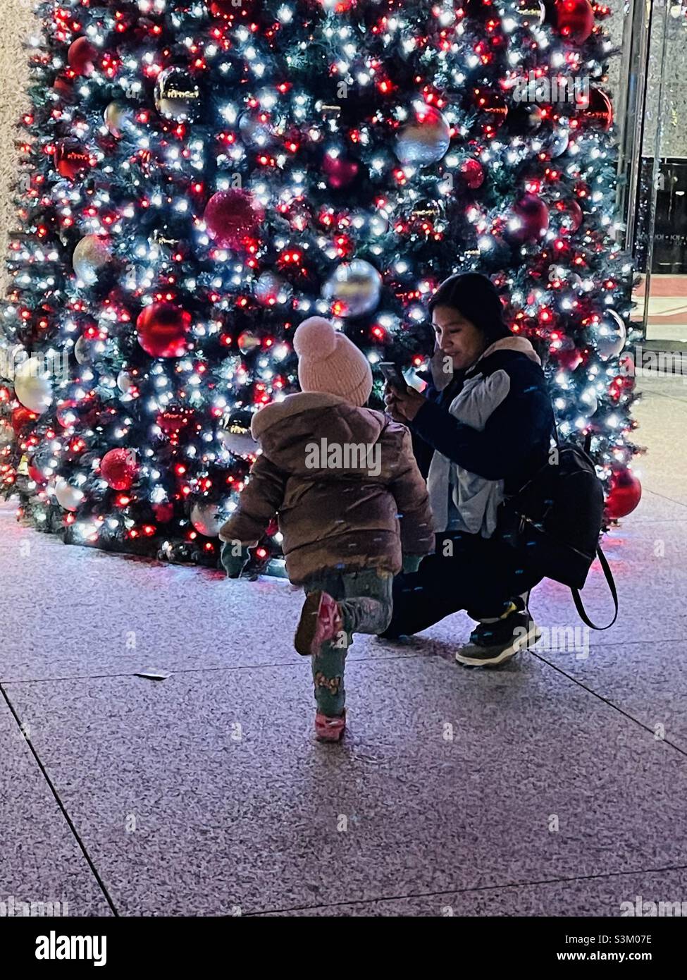 Eine Frau, die nachts in New York City mit einem Kind vor einem hellen Weihnachtsbaum ein Foto gemacht hat Stockfoto