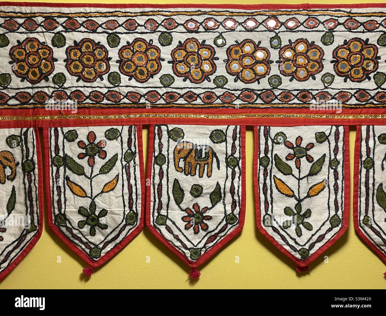 Eine indische Stickerei im traditionellen Stil mit Spiegelarbeiten, wie sie über einer Tür aufgehängt werden könnte. Zu den Motiven gehören Elefanten und Blumen Stockfoto