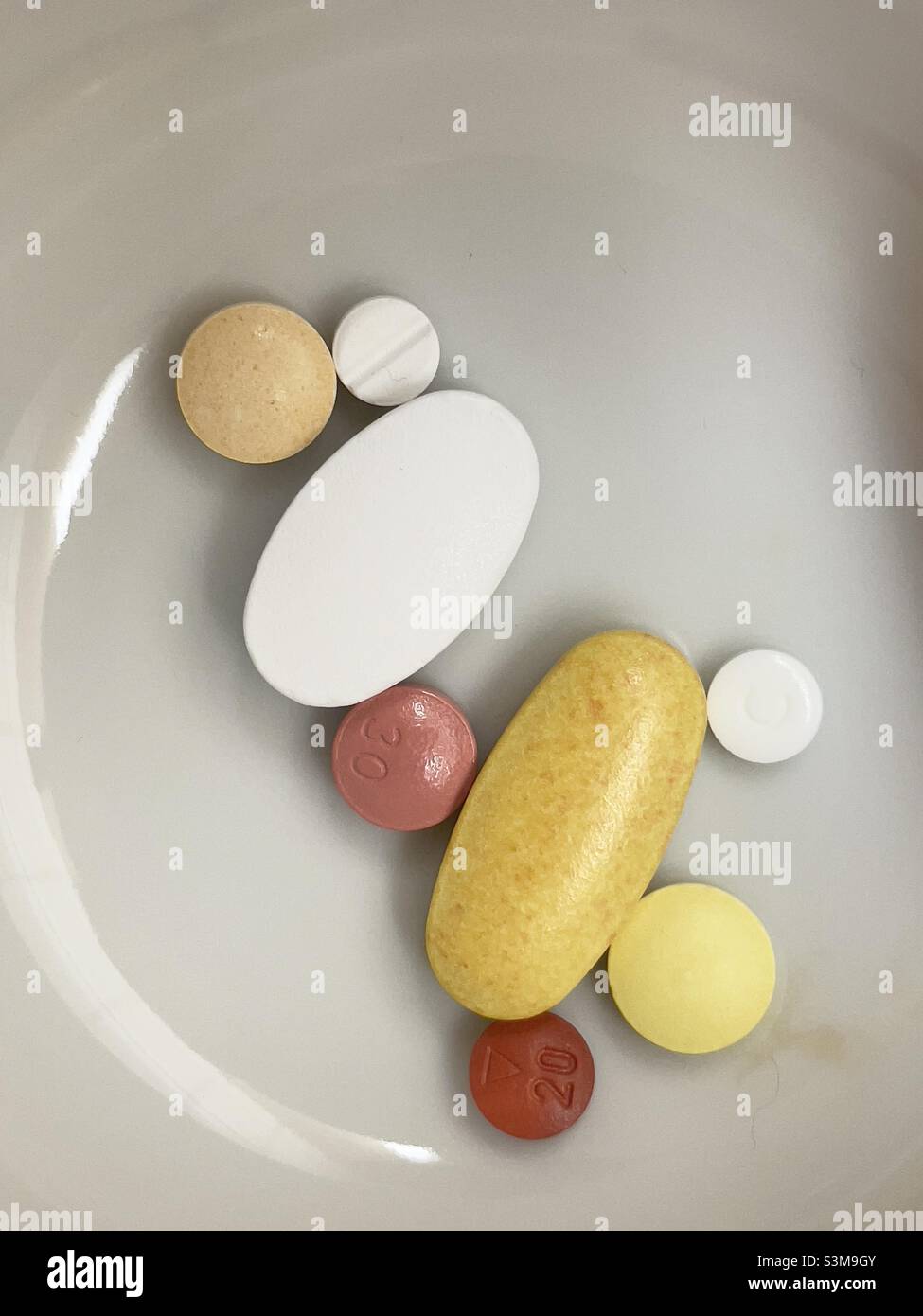 Eine Auswahl an runden und ovalen Tabletten und Tabletten in einer kleinen weißen Keramikschale - Smartphone-aufgenommenes Stockfoto