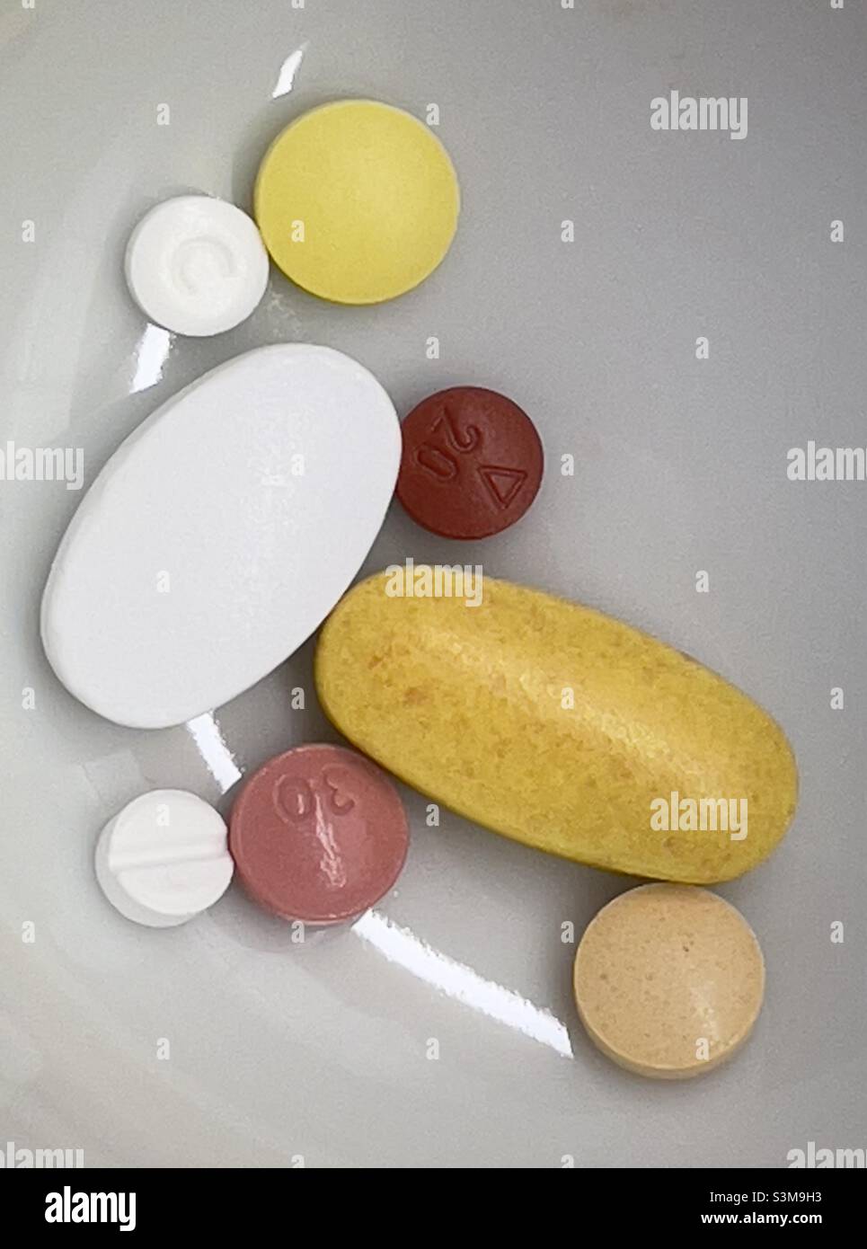 Eine Auswahl von Tabletten und Tabletten, rund und oval, in einer kleinen weißen Keramikschale - Smartphone-aufgenommenes Stockfoto
