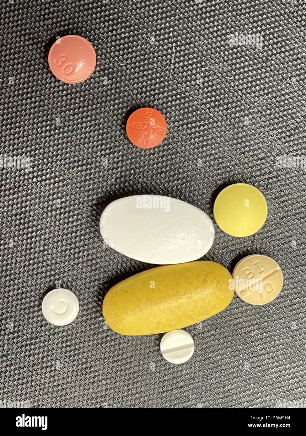 Eine Auswahl von Tabletten und Tabletten, rund und oval, auf einem strukturierten schwarzen Hintergrund - Smartphone-aufgenommenes Stockfoto