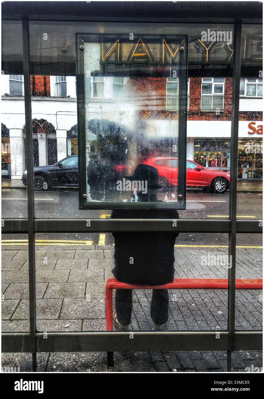 Mann in Hut wartet an der Bushaltestelle vor dem Everyman-Kino, Muswell Hill, London - Smartphone-aufgenommenes Stockfoto
