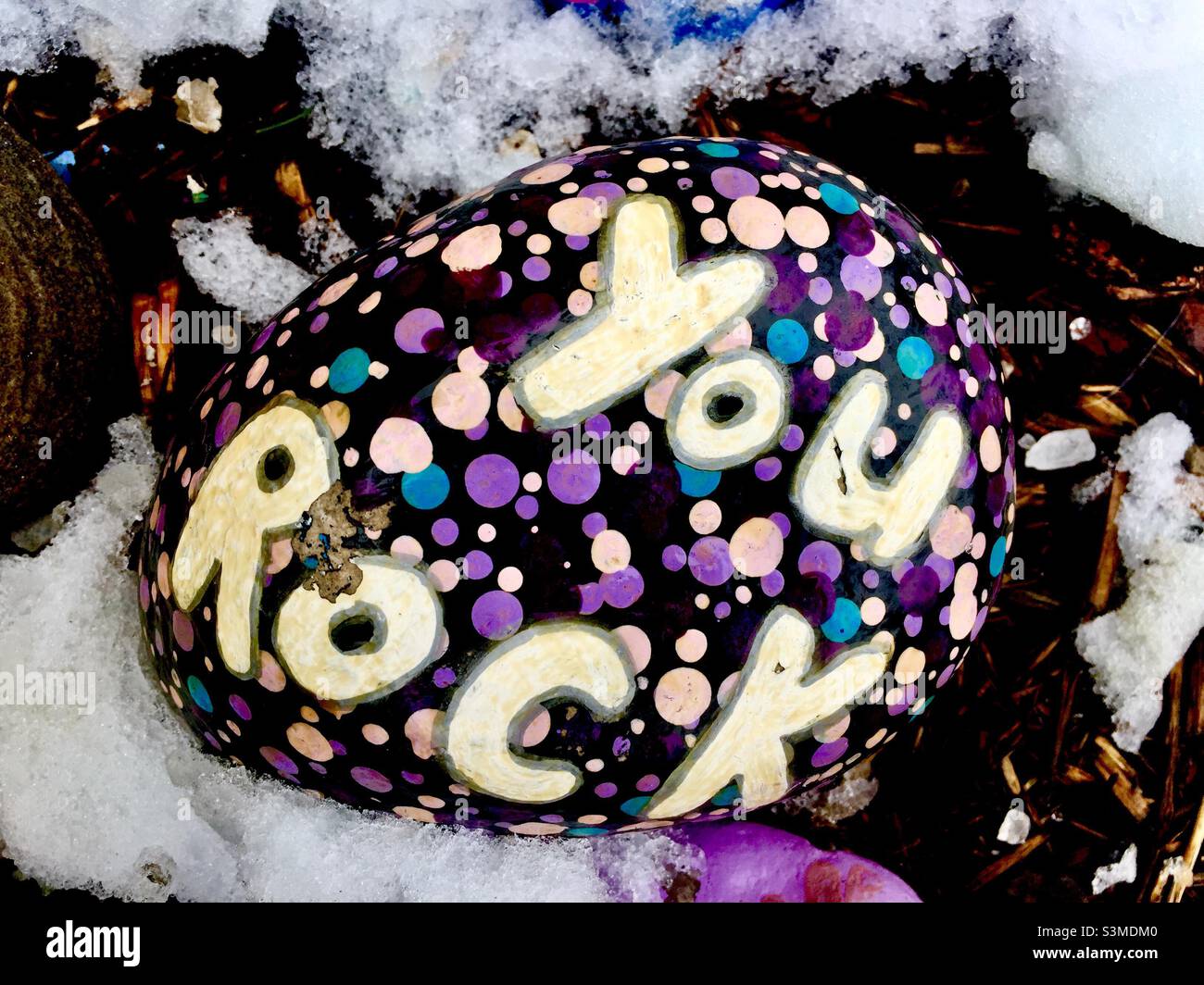 You Rock, Substantiv und Verb, gemalt auf einem kleinen Stein, im Schnee, im Freien, Ontario, Kanada. Gemälde auf Kieselsteinen, oft von Kindern gemacht, oder als Kunsttherapie für psychische Probleme. Stockfoto