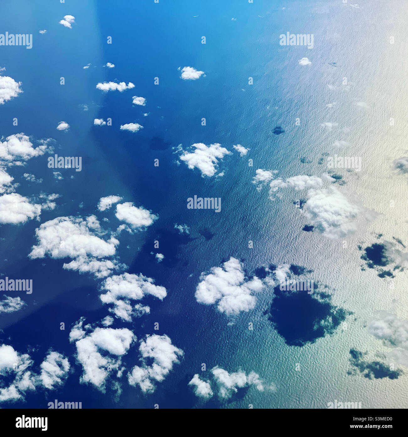 Wolken und ihre Schatten über dem Ozean von einem Flugzeugfenster aus gesehen - Smartphone-aufgenommenes Stockfoto
