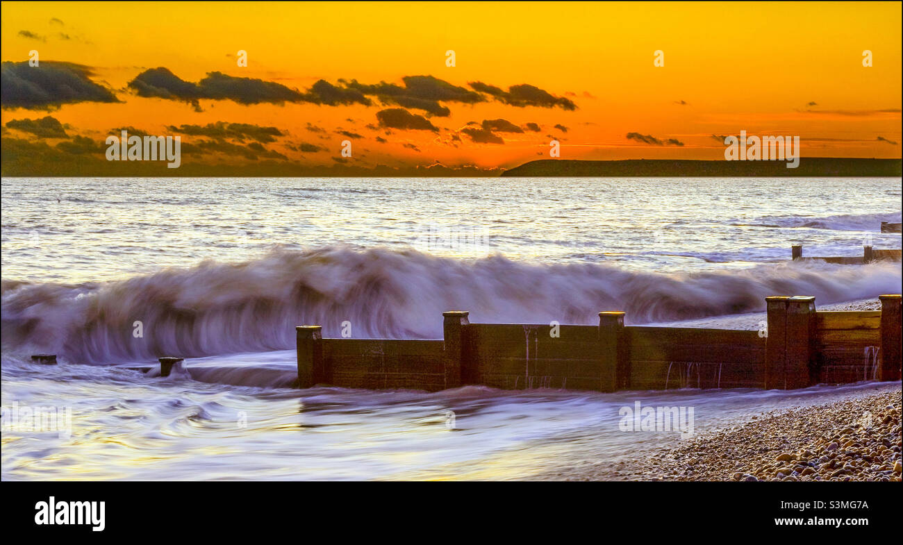 Unter einem leuchtend orangefarbenen Sonnenuntergang rollt eine Welle gegen die Küste Stockfoto