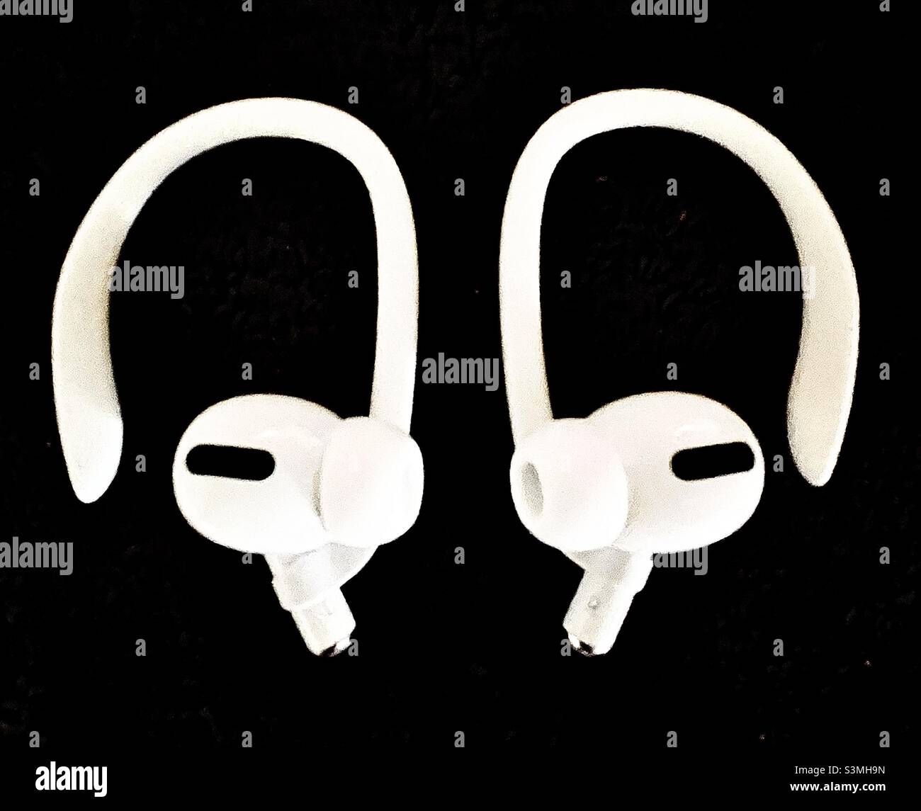 Das neueste Paar Apple AirPods Pro, mit angebrachten Ohrhaken, sitzt auf einem dunklen Hintergrund. Stockfoto