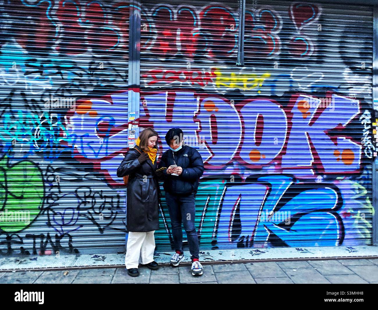 Ein junges Paar, das vor Graffiti stand, überdeckte Fensterläden. Stockfoto