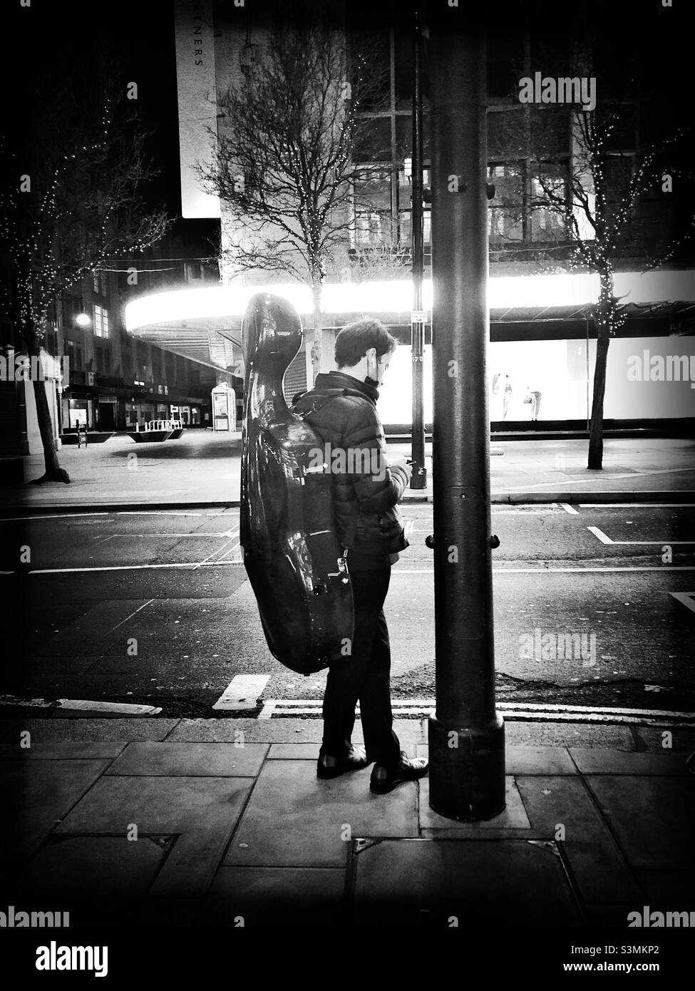 Mann, der an einer Bushaltestelle wartet, während er sein Instrument trägt Stockfoto